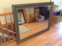 Full view of the large rectangular mirror leaning against stair railing showing overall condition and scale with floor and nearby furniture.