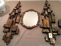 Overview of the ornate framed mirror centered between the two geometric resin wall hangings on a surface, showing overall design and scale.
