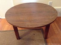 Full front view of oak round coffee table on hardwood floor and rug, showcasing its surface and legs.