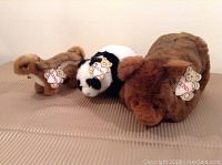 Three plush toys arranged on fabric surface: brown bear, black and white panda, and brown chipmunk, all with Gund brand tags.