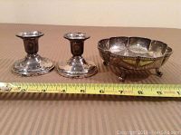 Overall view of two silver candlesticks and a silver footed bowl shown next to measuring tape for scale