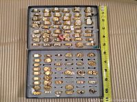 Two trays of gold-plated rings on foam inserts with a ruler for scale