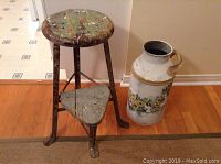 Old metal kitchen step stool and large metal milk can placed on hardwood floor against wall; stool shows worn paint and rust, milk can missing handle.