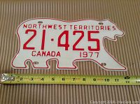 Front of the 1977 Northwest Territories polar bear shaped license plate with tape measure showing length of approximately 12 inches.