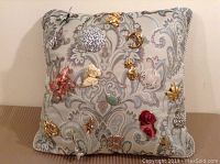 All 18 vintage brooches displayed on a decorative cushion showing a variety of shapes and finishes including floral, animal, moon, and heart designs.