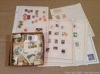 Photo showing loose and mounted mostly used stamps from around the world in a box and on postal sheets.