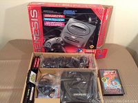 Photo of the Sega Genesis console, controllers, accessories, and original box showing branding and product details.