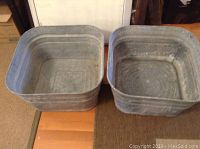 Two square galvanized metal laundry tubs stacked, showing signs of wear