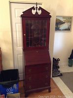 Full view of the tall Empire style desk china cabinet with decorative top, glass door, and wooden base with drawers.