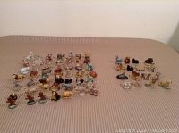 Wide view of 65 Wade ceramic figurines spread out on fabric surface showing two distinct groups: 49 tea figurines mostly intact, 16 bonus figurines to the right with visible chipping on some pieces.