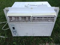 Front view of used White Black and Decker window air conditioner unit placed on grass showing vented front grille and control panel on left side.