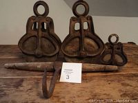 Front view of three metal barn pulleys with wooden rod and hook on wooden table.