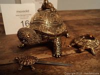 Gold-toned heavy brass turtle paperweight with amber crystal inlays, textured shell and legs, with accompanying small turtle letter opener and turtle magnifying glass on wood surface.