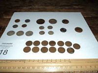 Photo of assorted Canadian, American, and British coins arranged on white paper with ruler
