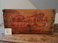 Front side of wooden Pepsi Cola crate showing faded red logo and French text displaying signs of wear and aging.