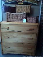 Front view of the dresser with four wicker baskets stacked on top, showing the dresser's natural pine finish, dovetail detail on drawers, and wooden handles.