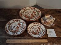 Top view of entire set including tea cup with saucer, salad plate, and two dinner plates showing the red and brown floral India Tree pattern.