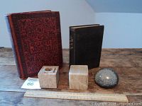 View of two vintage books and three paperweights on wooden surface with ruler for scale