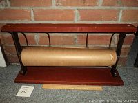 Paper cutter viewed from front showing roll of kraft paper and wooden base and top with cast iron supports.