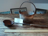 Rustic cast iron pot and leather-wrapped ladle placed on wood surface with ruler for scale.