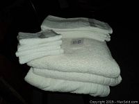 Stack of three folded white bath towels, two hand towels, and three face cloths stacked on top showing texture and size variety.