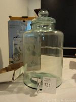 Side view of the large clear glass beverage dispenser with a rounded lid and metal spigot tap attached at the bottom front.