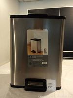 Front view of stainless steel rectangular waste bin showing label with bin product image and front foot pedal.