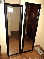 Front view of two black framed rectangular wall mirrors, one larger and one smaller, leaning against the wall.
