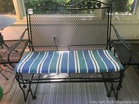 Front view of the wrought iron glider with striped blue, green, white, and brown seat cushion on a striped floor mat.