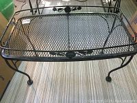 Rectangular wrought iron coffee table with mesh top, decorative accents on sides, curved legs