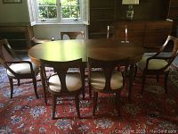 Full view of Walter Wabash dining table with six wooden chairs on a patterned rug, table extended with three leaves, positioned near a window