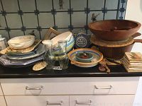Overview of wood salad bowl, ceramic and metal platters and bowls on countertop with wooden utensils and stone coasters.