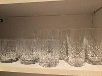 Shelf with several cut crystal glasses including two short tumblers with thick bases and multiple highball glasses with intricate cut designs.