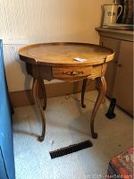 View of round wooden table with drawer and curved legs, showing top and drawer front.