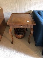 Front view of the wooden side table showing cabriole legs and basket underneath.