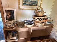 Shelf with two hand-painted ceramic bowls with yellow and blue decorative designs and a clear faceted glass bowl. Stack of woven baskets of different sizes and shapes with one basket having a handle on top.