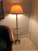Full view of 58-inch tall brass floor lamp with pleated fabric lampshade and round glass table surface in middle.