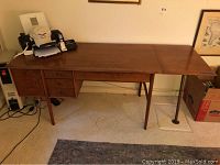 Desk in room against wall showing full length top, left cabinet door closed, right support leg