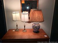 Front view of two brass finish lamps and one ceramic floral lamp on wood table