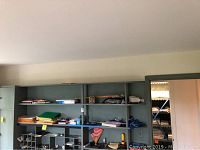 Shelves in a hallway linen closet containing assorted office supplies on the lower shelves, and bed linens folded and stacked on the upper shelves.