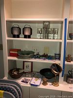 Wide view of shelf showing lanterns, glass candleholders, ceramic bowls, trays, ornate vanity mirror and wind-up toys