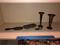 Five sterling silver items displayed on a shelf including two vases, a spoon, a dish, and a brush.