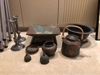 Overview of the entire lot showing all items arranged on carpet: two metal candleholders, bronze vessel on wooden base, clay teapot with handle, two small metal pots, two metal bells without clappers, and one metal bowl.