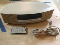 Full view of beige Bose Wave Radio III with remote and power cord next to it on a wooden surface.