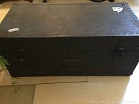 Front view of black steamer trunk with metal clasps and central lock.