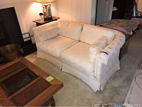 Cream upholstered love seat with two removable seat and back cushions, curved arms, and straight skirted base.