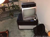 Photo of Toshiba TV and VCR combo unit on top of a black MDF TV stand with glass front drawer and shelves, showing the overall setup.