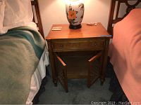 Front view of wooden night stand showing single top drawer, cabinet doors closed, situated between two beds.