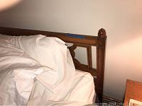 Side view of one wooden headboard with attached bed frame partially covered in bedding, showing turned post and decorative carved panel with circular floral inlays.