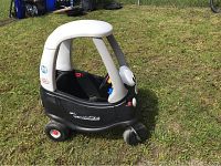 Side angle view of the black and white Little Tikes police pedal car on grass, showing one side wheel and structural design.